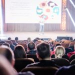 Público acompanha atentamente uma apresentação em um auditório durante uma conferência.