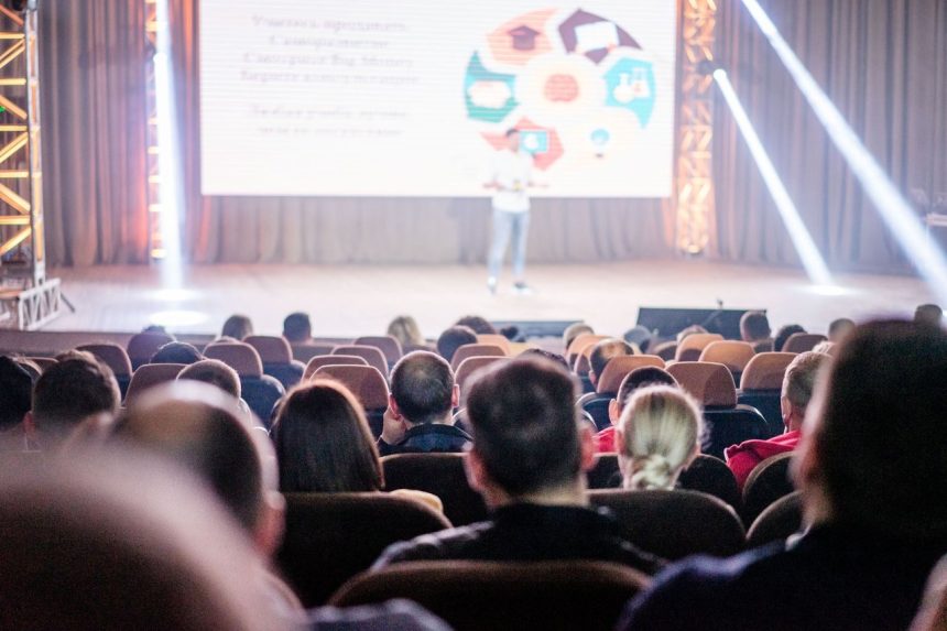 Público acompanha atentamente uma apresentação em um auditório durante uma conferência.