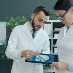 Dois médicos analisam a radiografia de um paciente em um tablet, em um consultório.