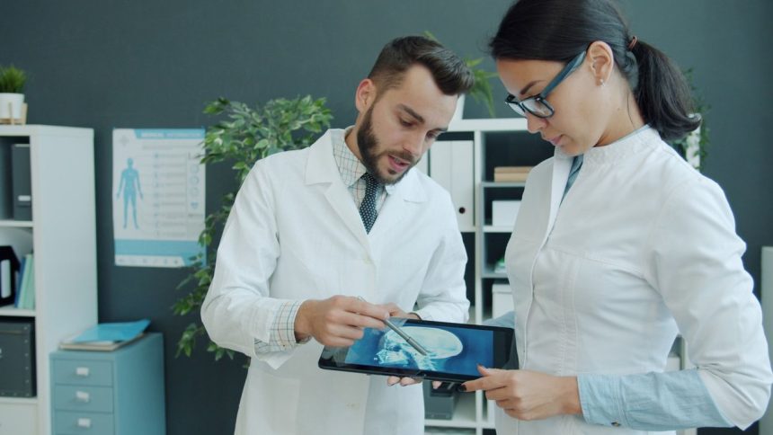 Dois médicos analisam a radiografia de um paciente em um tablet, em um consultório.