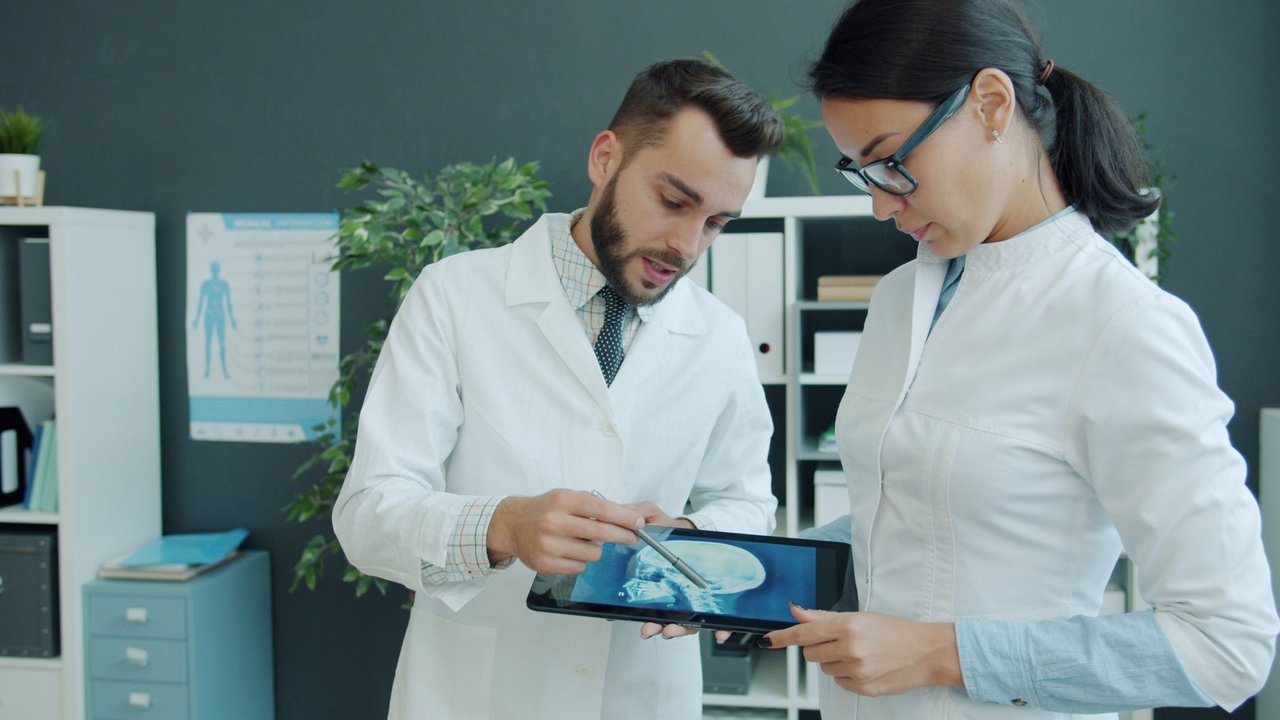 Dois médicos analisam a radiografia de um paciente em um tablet, em um consultório.