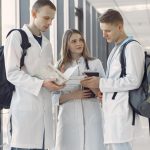 Três estudantes de medicina compartilham anotações e estudam juntos no corredor de um hospital.