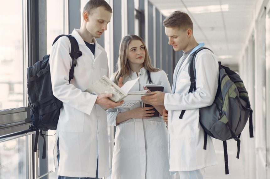 Três estudantes de medicina compartilham anotações e estudam juntos no corredor de um hospital.