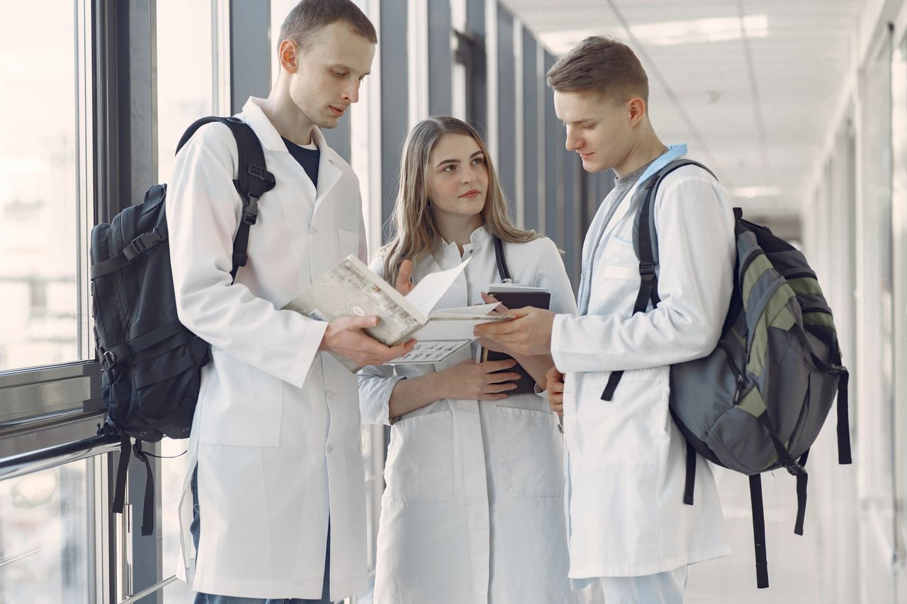Três estudantes de medicina compartilham anotações e estudam juntos no corredor de um hospital.