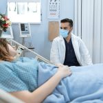 Médico usando máscara conversa com paciente internado em um leito hospitalar.