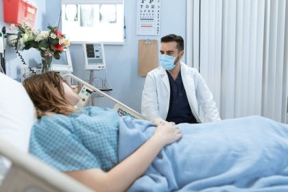 Médico usando máscara conversa com paciente internado em um leito hospitalar.