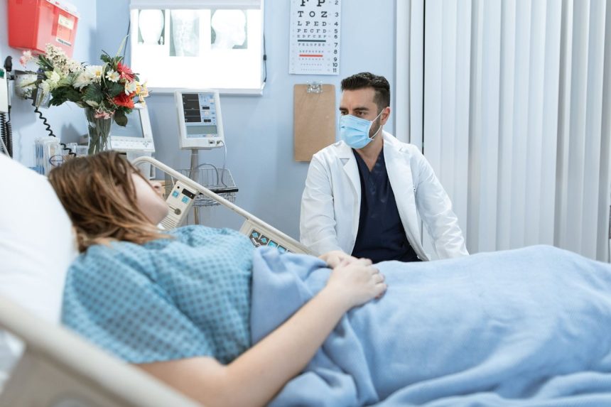 Médico usando máscara conversa com paciente internado em um leito hospitalar.