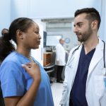 Profissionais de saúde conversam em um corredor de hospital sobre o atendimento a pacientes.